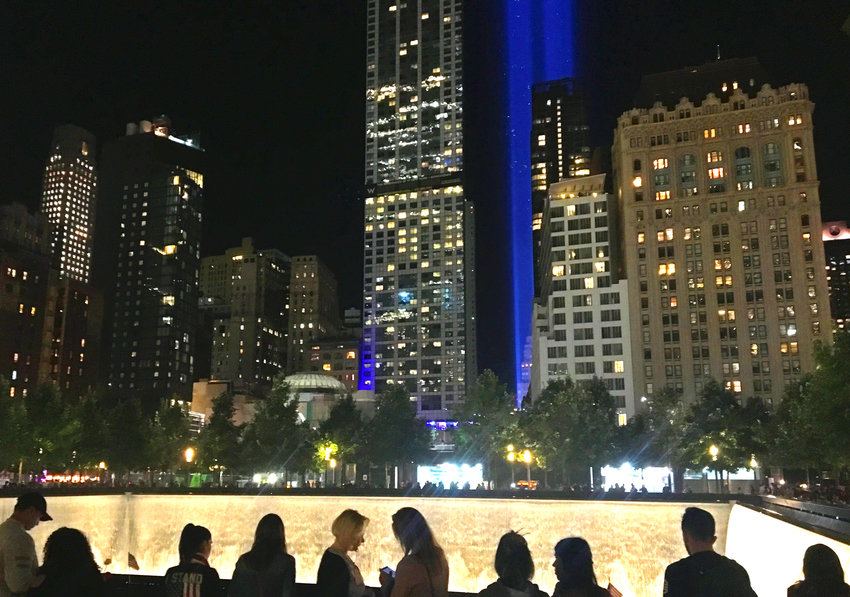 A crowd gathers at the twin memorial fountains at the World Trade Center site in Lower Manhattan, New York, as twin blue beacons pierce the night sky on Sept. 11, 2017.